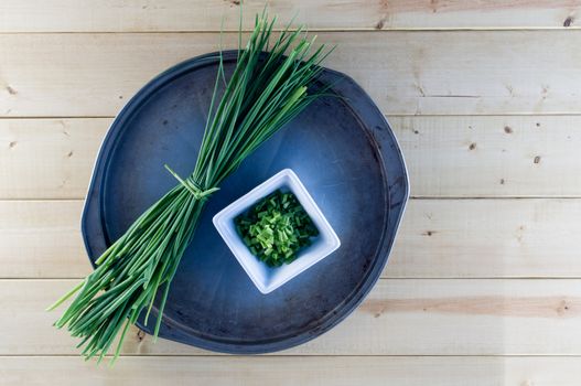 Fresh chives on vintage baking sheet, with rustic plank background