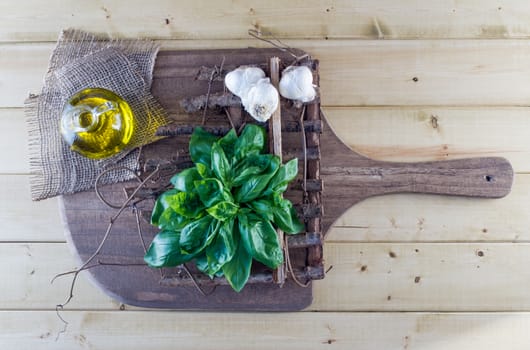Fresh basil leaves, olive oil, and garlic bulbs on rustic board