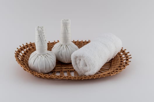 Thai herbal massage balls and rolled white spa towel in wicker tray