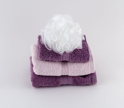Pink and lavender folded spa towels and white bath pouf
