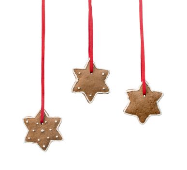 Gingerbread stars hanging on red ribbons against white background.
