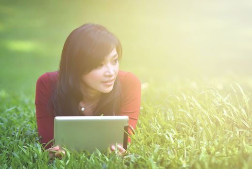 pretty woman using tablet outdoor laying on grass with flare light