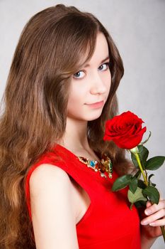 Closeup portrait of a young attractive woman with a red rose over grey background