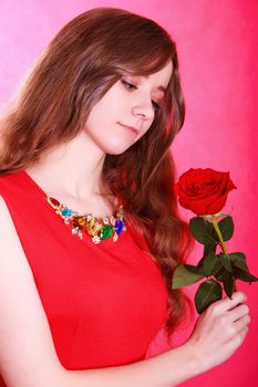 Portrait of a young attractive woman with a red rose over pink background