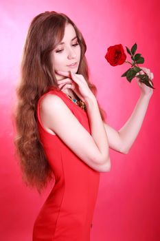 Portrait of a young attractive woman with a red rose over pink background