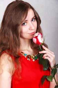 Portrait of a beautiful young woman with a red rose over grey background