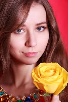 Portrait of a beautiful young woman with a yellow rose over pink background