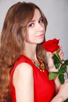 Beautiful young woman with a red rose over grey background