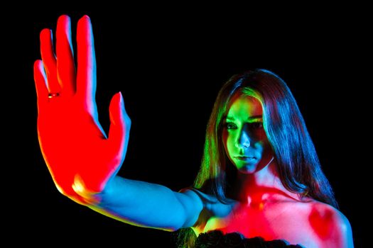 Beautiful young woman in red, green and blue lights showing the stop sign over black background