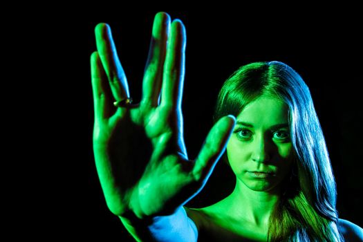 Beautiful young woman in green light showing the alien sign over black background