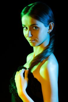 Beautiful young woman in yellow, green and blue lights over black background