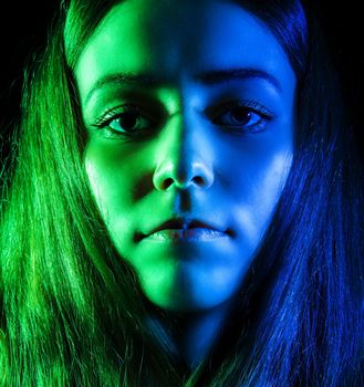 Beautiful young woman in green and blue lights over black background