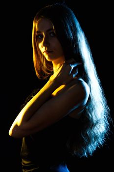 Beautiful young woman in blue and yellow lights over black background