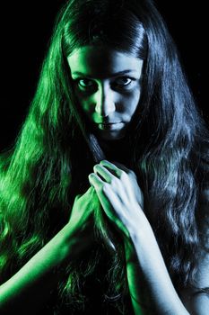 Scary face of a young woman in green and grey lights over black background