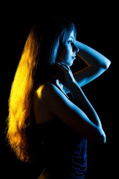 Beautiful young woman in blue and yellow lights over black background