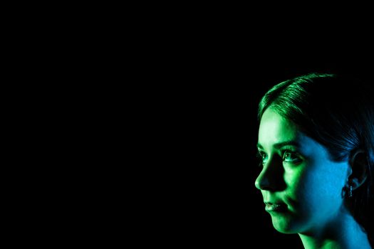 Beautiful young woman's face in blue and green lights at the corner over black background