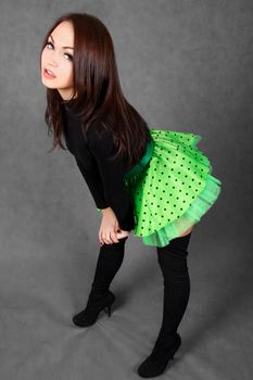 Portrait of a young attractive woman in a bright green skirt over grey background