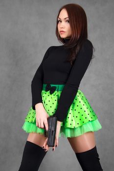 Portrait of a young attractive woman in a bright green skirt with a gun over grey background