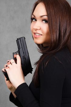 Portrait of a young attractive woman with a gun over grey background