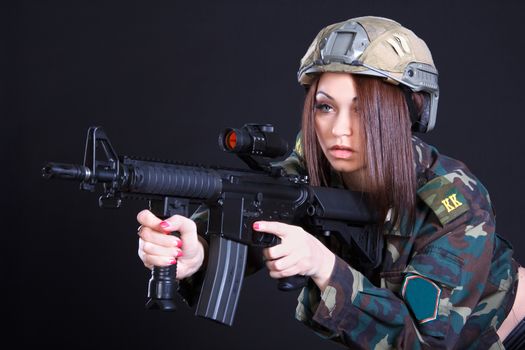 Portrait of a woman in a military uniform with an assault rifle over black background