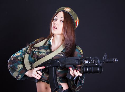 Beautiful young woman in a military uniform with an assault rifle over black background