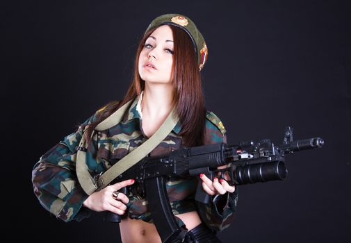 Young woman in the military uniform with the assault rifle over black background