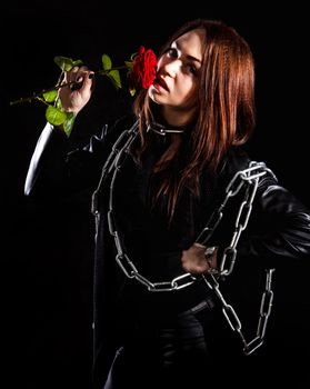Beautiful young woman with chains and a red rose over black background