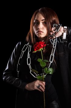 Beautiful young woman with chains and a red rose over black background