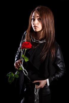 Beautiful young woman with chains and a red rose over black background