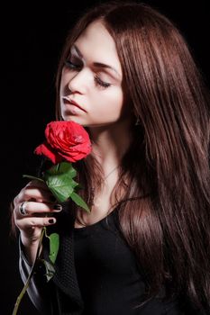 Closeup portrait of a pale beautiful young woman with a red rose over black background