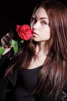 Closeup portrait of a pale beautiful young woman with a red rose over black background