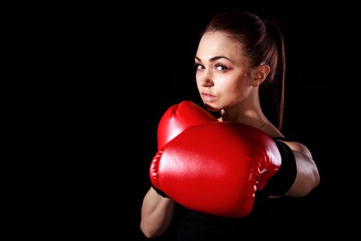 Beautiful young woman in red boxing gloves over black background