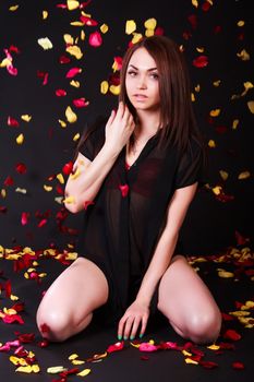 Beautiful young woman sitting under the falling petals over black background