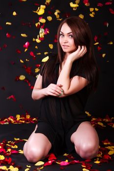 Beautiful young woman sitting under the falling petals over black background