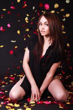 Beautiful young woman sitting under the falling petals over black background