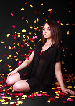 Beautiful young woman sitting under the falling petals over black background