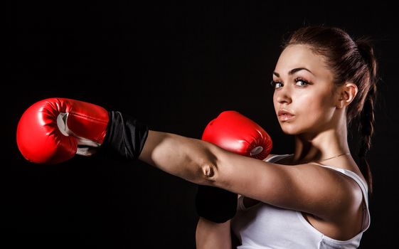 Beautiful young woman in a red boxing gloves over black background