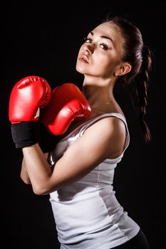 Beautiful young woman in a red boxing gloves over black background