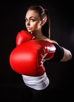 Beautiful young woman in a red boxing gloves over black background (focus is on the glove)