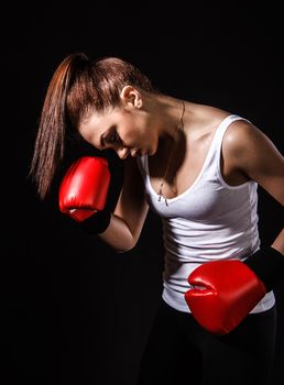 Beautiful young woman in a red boxing gloves over black background