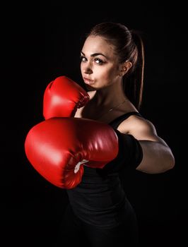 Beautiful young woman in a red boxing gloves over black background