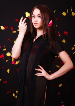 Beautiful young woman under the falling petals over black background
