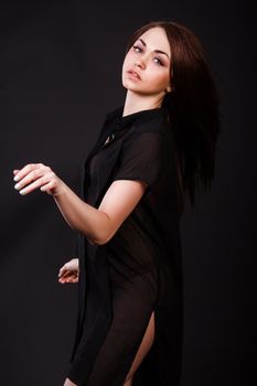 Amazing young woman in a red underwear and a black peignoir with a flying hair over black background