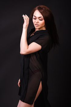 Amazing young woman in a red underwear and a black peignoir with a flying hair over black background