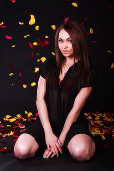 Beautiful young woman sitting under the falling petals over black background