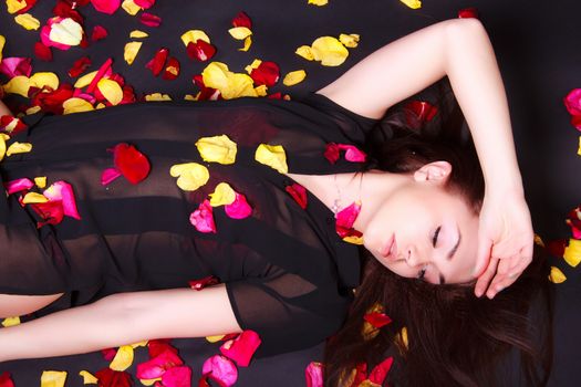 Beautiful young woman laying on sparse rose petals over black background