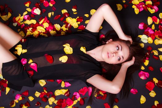 Beautiful young woman laying on sparse rose petals over black background