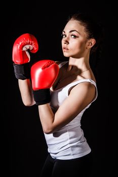 Beautiful young woman in a red boxing gloves over black background