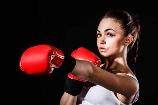 Beautiful young woman in a red boxing gloves over black background