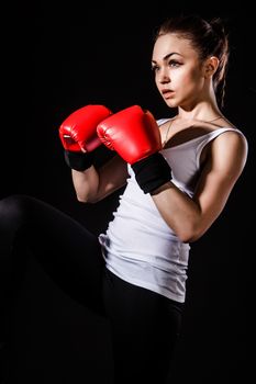 Beautiful young woman in a red boxing gloves over black background